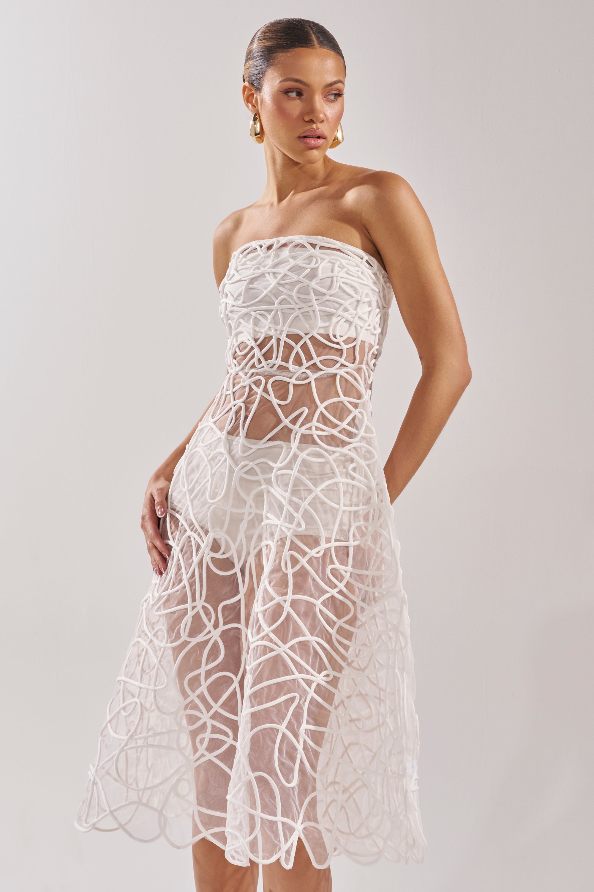 The MAYA ABSTRACT MIDI DRESS IN WHITE features a strapless sheer midi silhouette with swirling abstract lines over a short white underlay—an elegant pick for any cocktail party. 3
