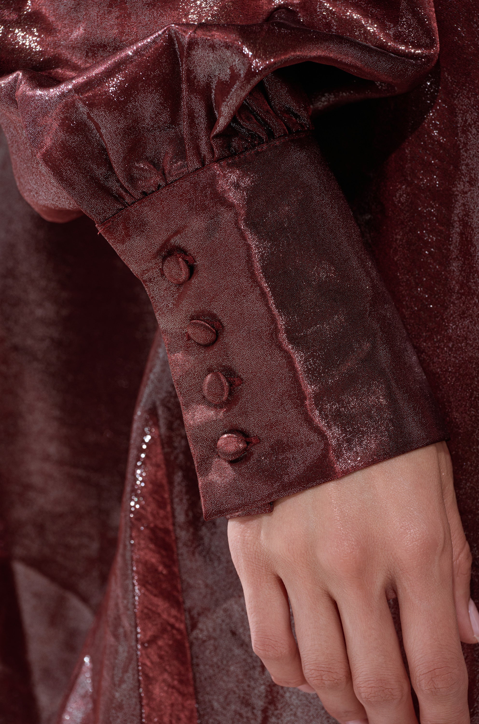 A close-up of a hand resting on the shiny, deep red sleeve of the LENNON PLUNGING SATIN SHIRT DRESS, showcasing four matching fabric-covered cuff buttons.