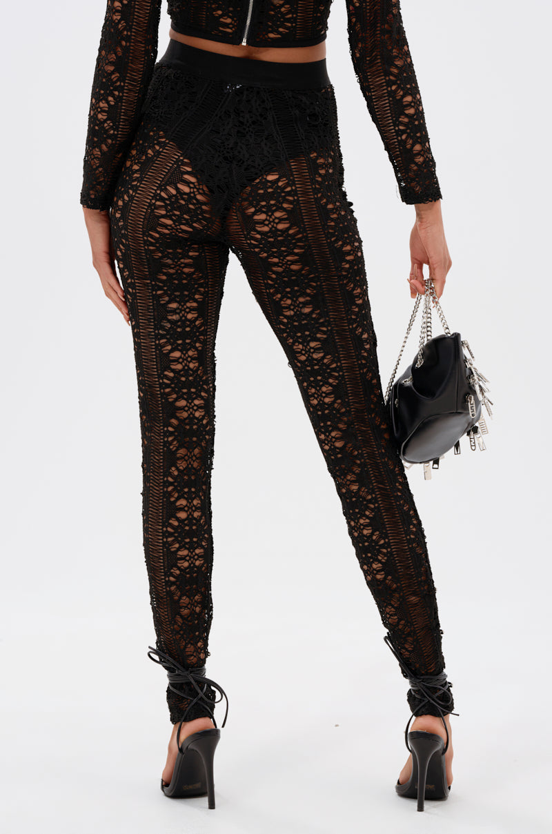 A person wears the TRY ME LACE LEGGING—a sheer black lace jumpsuit—with black high heels, styled with a small black handbag featuring silver accents, standing with their back to the camera.