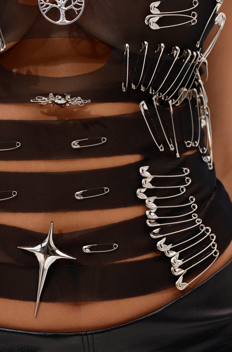 The TRY ME DISTRESSED TANK is a black mesh crop top featuring edgy silver safety pins in various sizes and a bold star-shaped metallic accent, with skin peeking through its horizontal fabric cutouts.