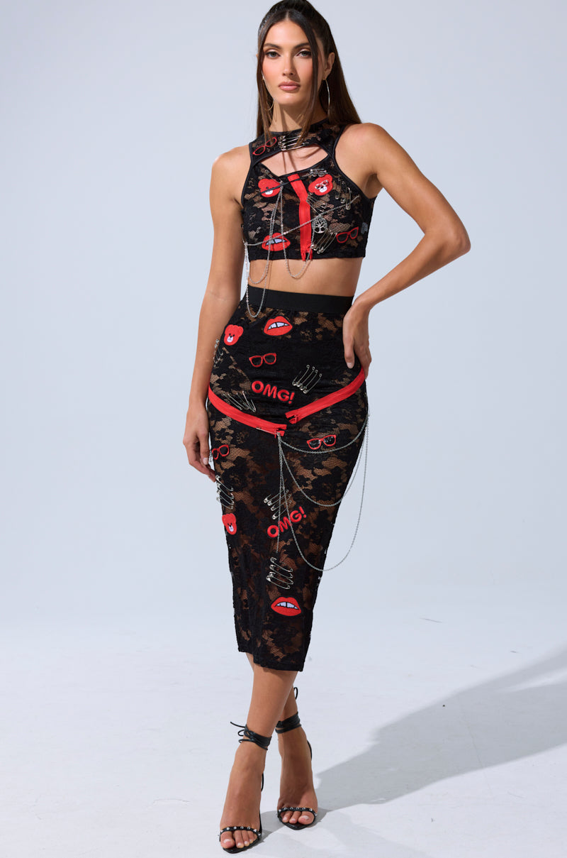 A woman models the OMG LACE TANK WITH EMBELLISHMENTS, a black lace two-piece featuring red and white graphic prints like lips and "OMG!", styled with strappy high heels and silver chain accessories on a plain light background.