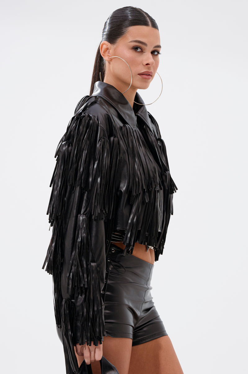A woman with long dark hair in a sleek ponytail wears large hoop earrings and the SIERRA TASSEL MOTO jacket with matching high-waisted shorts, confidently looking to the side against a plain background.