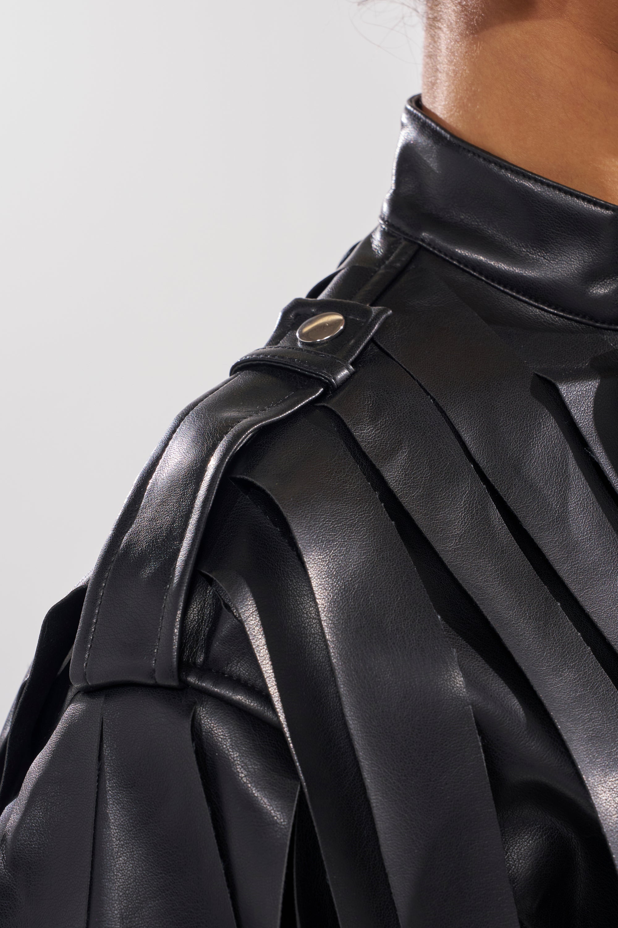 Close-up of a person wearing the GONE WEST STRAPPY MOTO, a black cropped moto jacket featuring a high collar, layered fringed shoulder details, and metallic snap button closure.