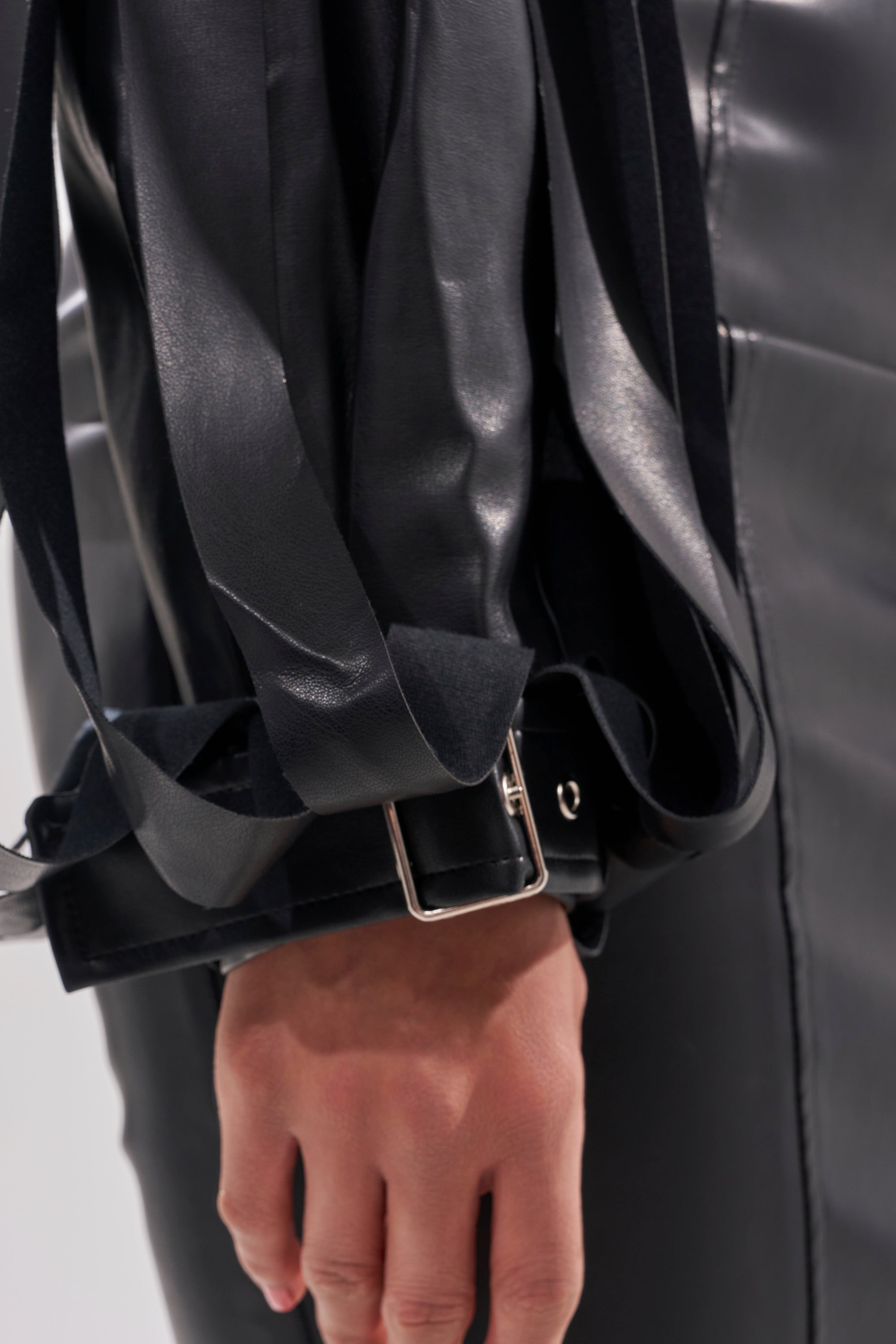 A person wearing the GONE WEST STRAPPY MOTO jacket, with a close-up on their hand, arm, and a wide belt adorned with a silver buckle and long, trailing leather straps.