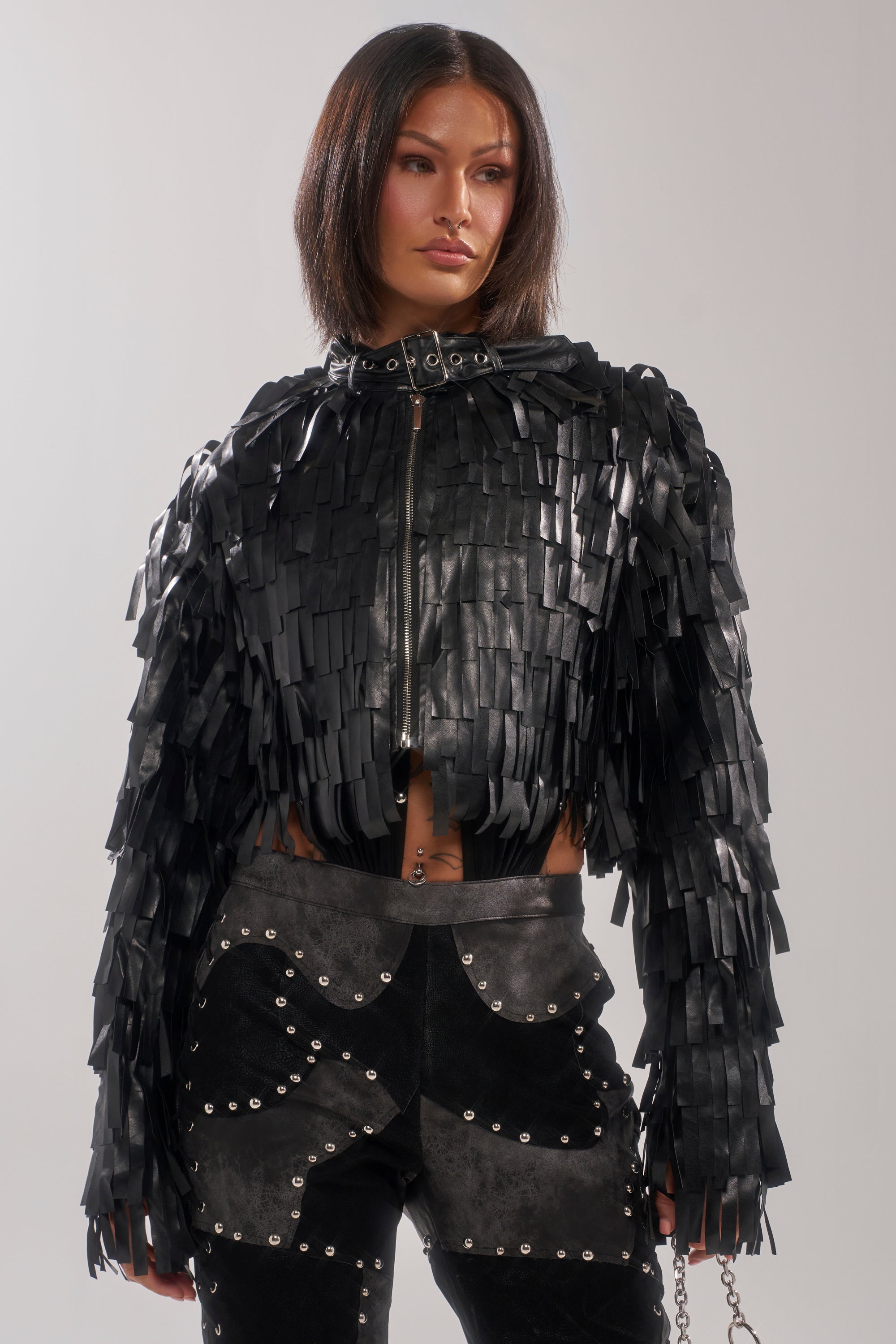 A woman with straight dark hair wears the RIDE EM FRINGE MOTO jacket and black studded pants, standing against a plain light background.