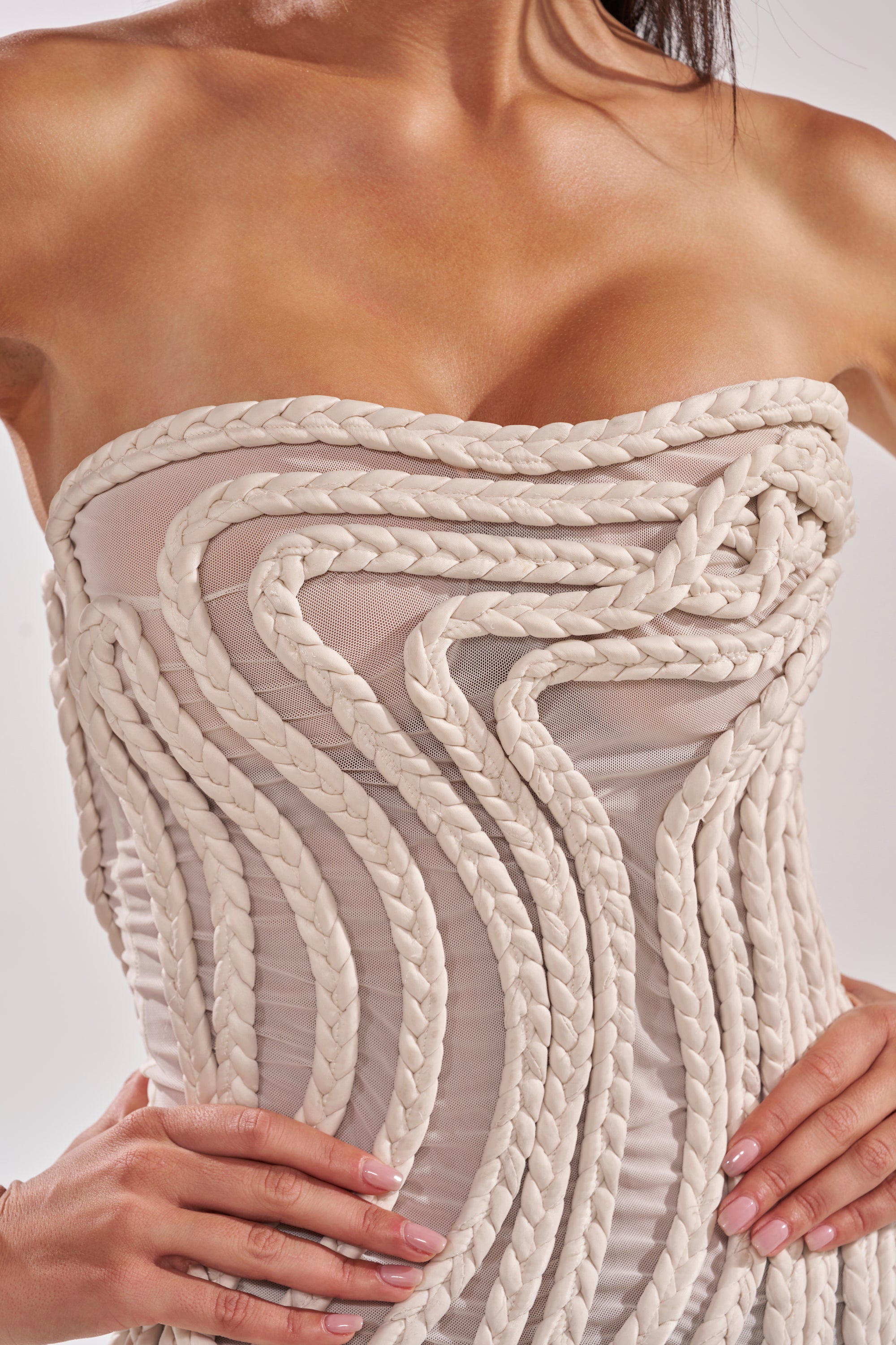 A close-up shows a woman in the ALL OVER THE PLACE BRAIDED MIDI DRESS IN IVORY, featuring strapless styling and thick, sculptural ivory braids that create a wavy, three-dimensional effect as she poses with her hands on her hips. 7