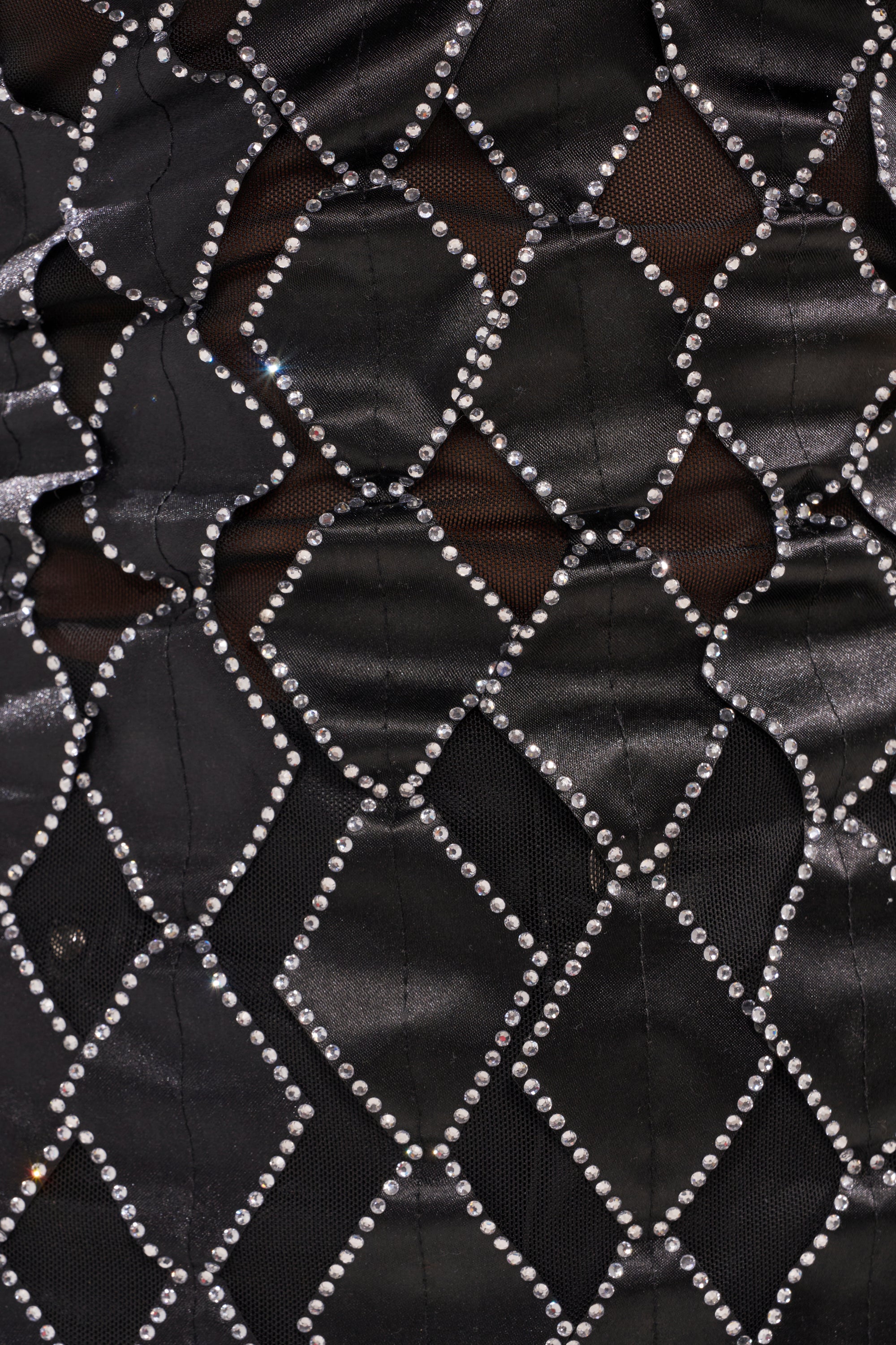Close-up of the ELINA SATIN TOP, a black satin top featuring diamond-shaped mesh panels outlined with sparkling rhinestone trim and sheer details. 5