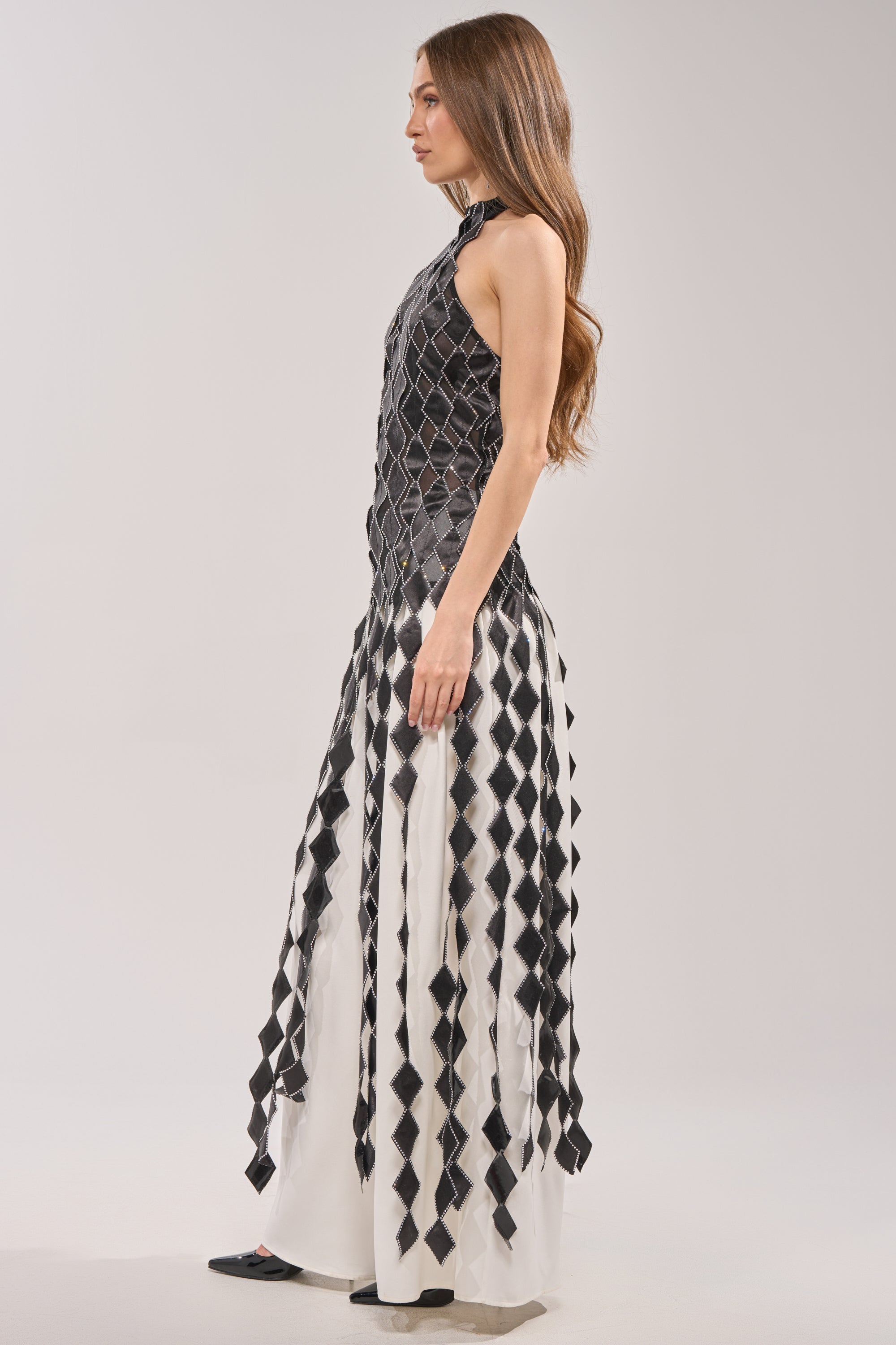 A woman with long brown hair stands in profile against a light background, wearing the ELINA SATIN TOP—a sleeveless, black and white geometric-patterned top with rhinestone trim and a fitted silhouette. 5