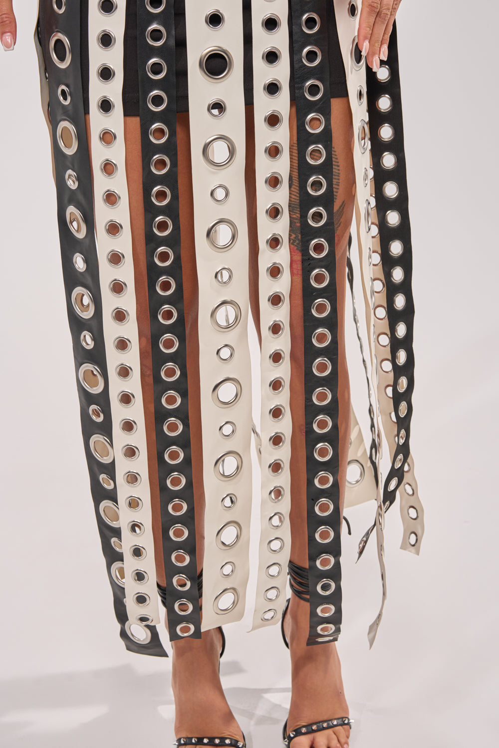 A close-up of a person wearing the ON MY BEST BEHAVIOR TASSEL MAXI DRESS, designed with alternating black and beige vertical strips, paired with black high-heeled sandals adorned with silver studs. 5