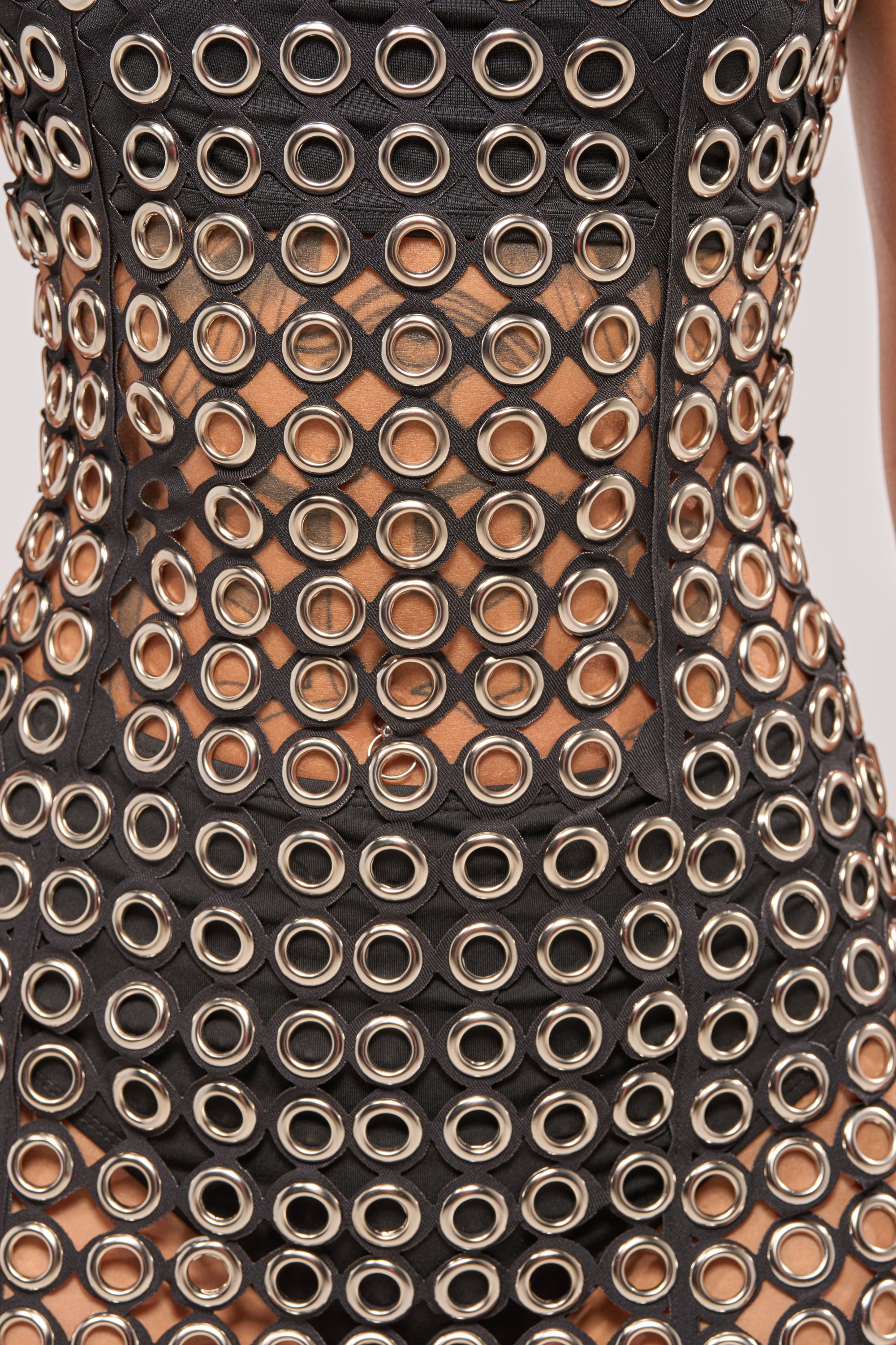 A close-up of the FLIRT ALERT CHAIN MIDI DRESS, a sheer black midi dress featuring large metallic eyelets in a grid pattern that reveals skin underneath. 6