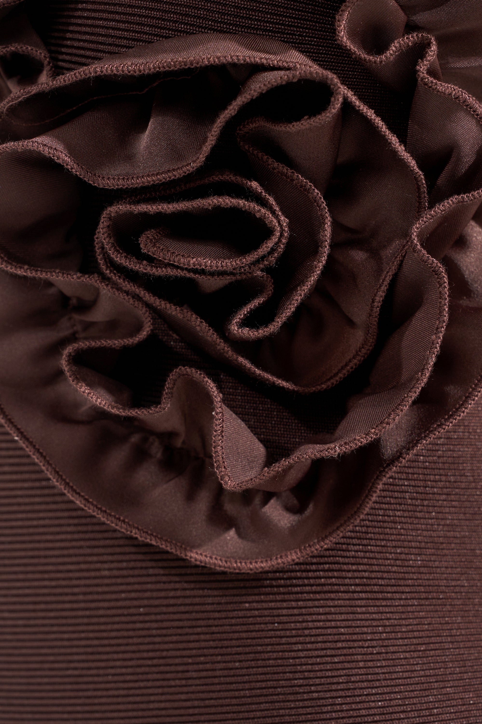 Close-up of the STANDING OVATION FLOCKED MAXI DRESS IN CHOCOLATE, featuring ruffled pleats, a flower-inspired center design, and smooth edges—ideal for elegant evening wear. 4