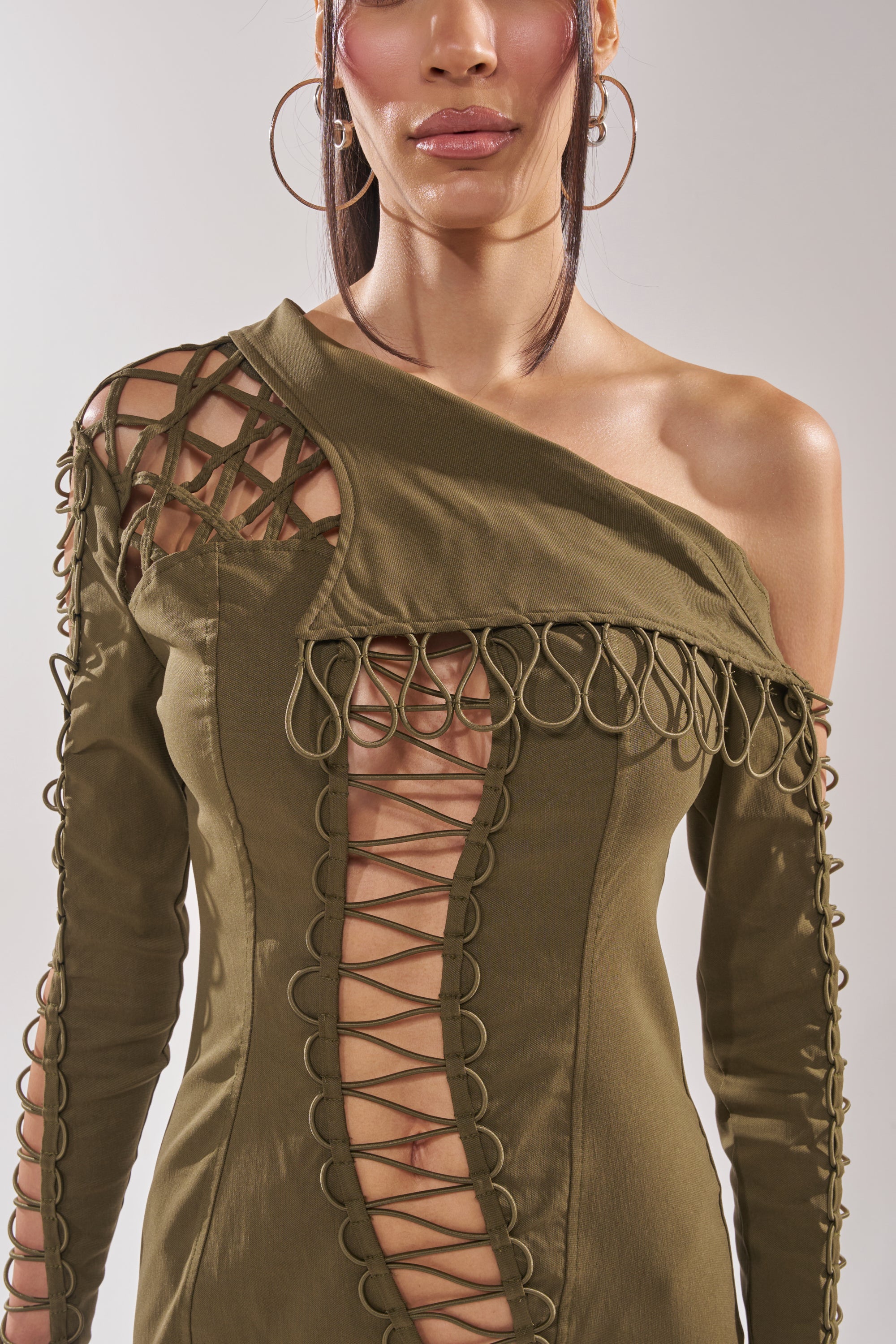 Wearing the LACED UP MINI DRESS in olive, featuring looped and crisscrossed cutout details on the front and sleeve, a person stands against a neutral background. 9