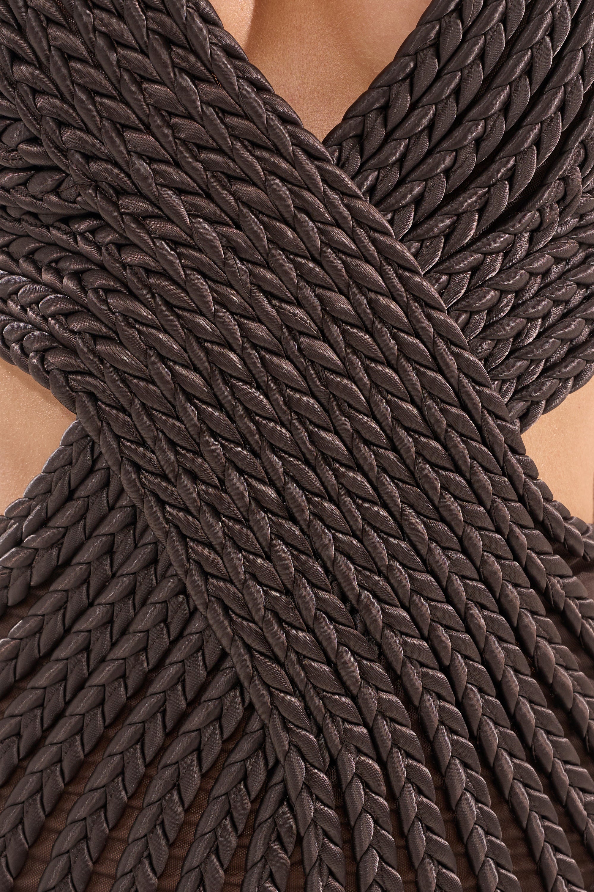 Close-up of the INTENTIONALLY CLOSE BRAIDED MINI DRESS IN BROWN, featuring intricately braided dark brown material in a crisscross pattern against bare skin for added texture and elegant detail—perfect as a chic wedding guest dress. 4