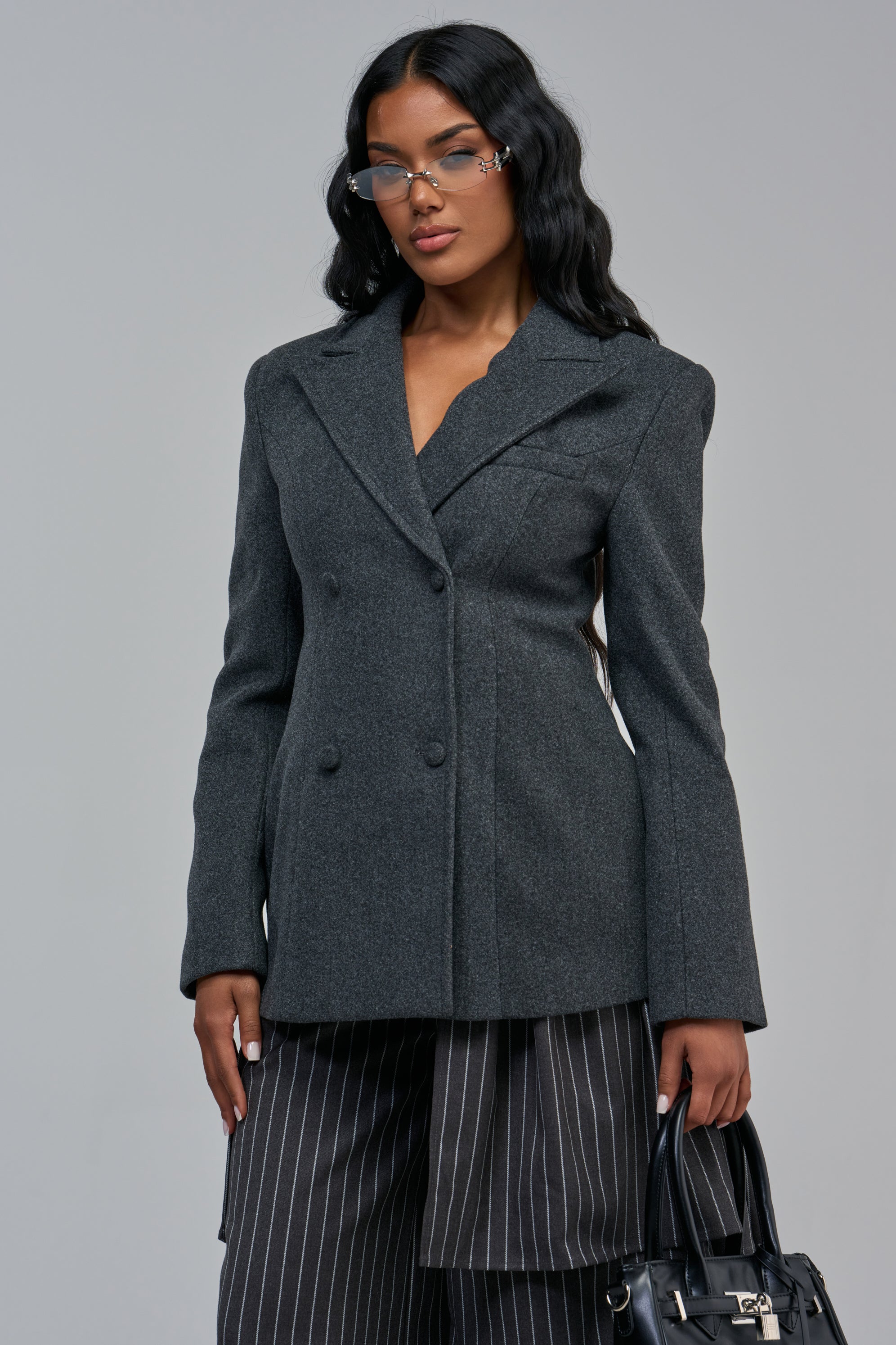 A person wearing a charcoal grey FAWN LACE UP BLAZER with pinstriped trousers and holding a black handbag, styled for business casual officewear.
