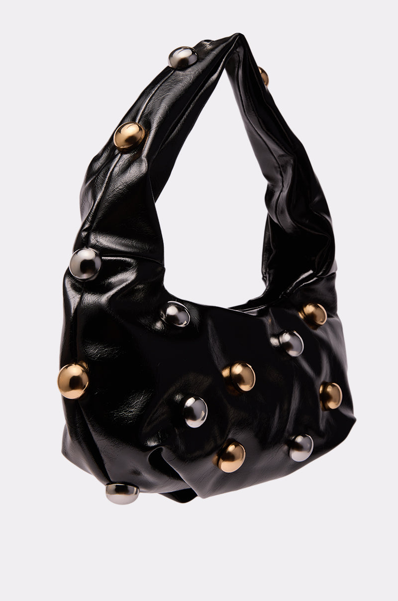 The TOO MOD BALL PURSE is a black, shiny faux leather baguette bag with a twisted handle and bold gold and silver metallic studs, creating a chic look against any plain light background. 2
