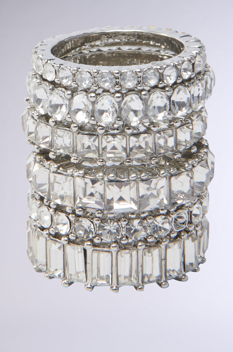 The SPEND IT RHINESTONE RING SET features five silver-tone bands, each adorned with clear gemstones in various shapes, creating a sparkling, layered look and dazzling stacking shine.