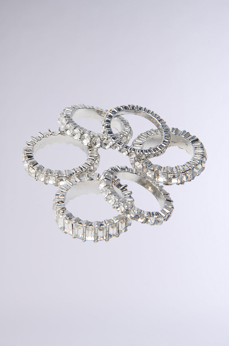 Six silver-tone bands from the SPEND IT RHINESTONE RING SET, each with clear rectangular gemstones, are arranged in a loose cluster on a light gray background. These shiny, faceted rings are photographed from above and perfect for stacking.