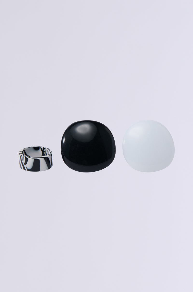 Three items are showcased on a light gray background: the ITS BLACK AND WHITE RING SET with a metallic dome-shaped ring on the left, a glossy black circular stone in the middle, and a smooth white circular stone on the right.
