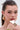 A woman with sleek, dark hair pulled back wears large, shiny gold earrings and the bold MOD LIFE RING—a wide, angular statement piece—resting her chin on her hand to highlight their modern style against a neutral background.