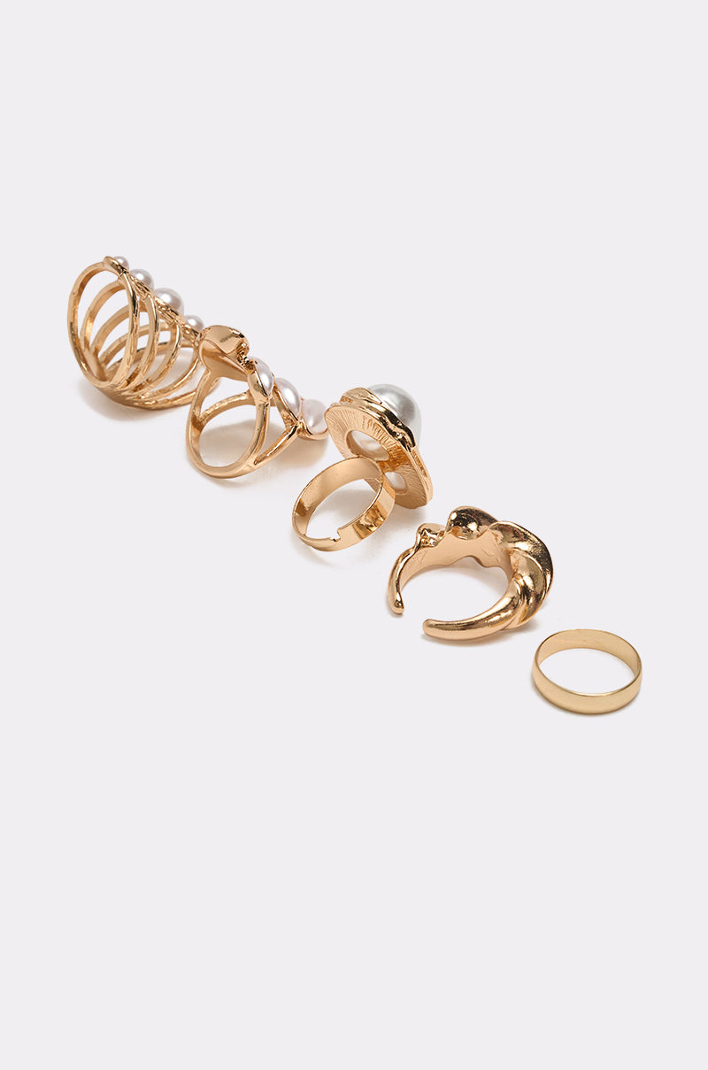 The VANJA RING SET features five stacked rings arranged in a row on a plain white background, combining vintage-inspired textures and pearls with simple, smooth bands. 3