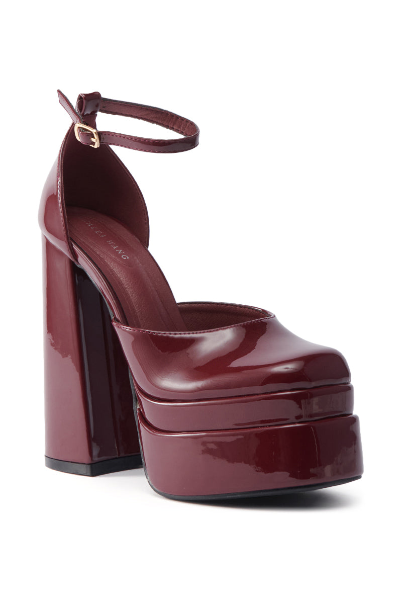 The AZALEA WANG YUFFIE PATENT BURGUNDY PUMP features a glossy burgundy finish, platform sole, chunky heel, rounded toe, and an ankle strap with a small buckle.