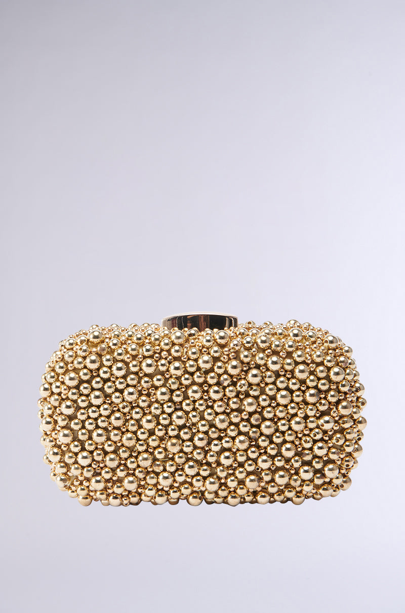The POPPIN BUBBLY EMBELLISHED CLUTCH is a gold clutch purse adorned with numerous small, shiny gold beads. It features a rectangular shape with rounded edges and a flat base, showcasing a metallic gold hardshell and a gold clasp at the top against a plain white background. 1