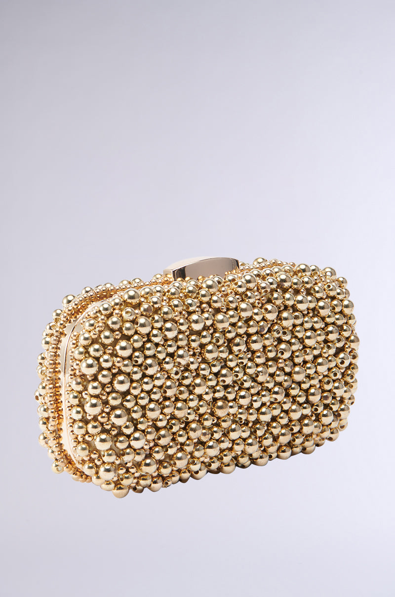 The POPPIN BUBBLY EMBELLISHED CLUTCH is a small, rectangular gold clutch purse beautifully decorated with countless shiny gold beads, crafting a textured and opulent exterior. It boasts a metallic gold hardshell with an understated clasp at the top and includes a detachable chain link shoulder strap for enhanced convenience.