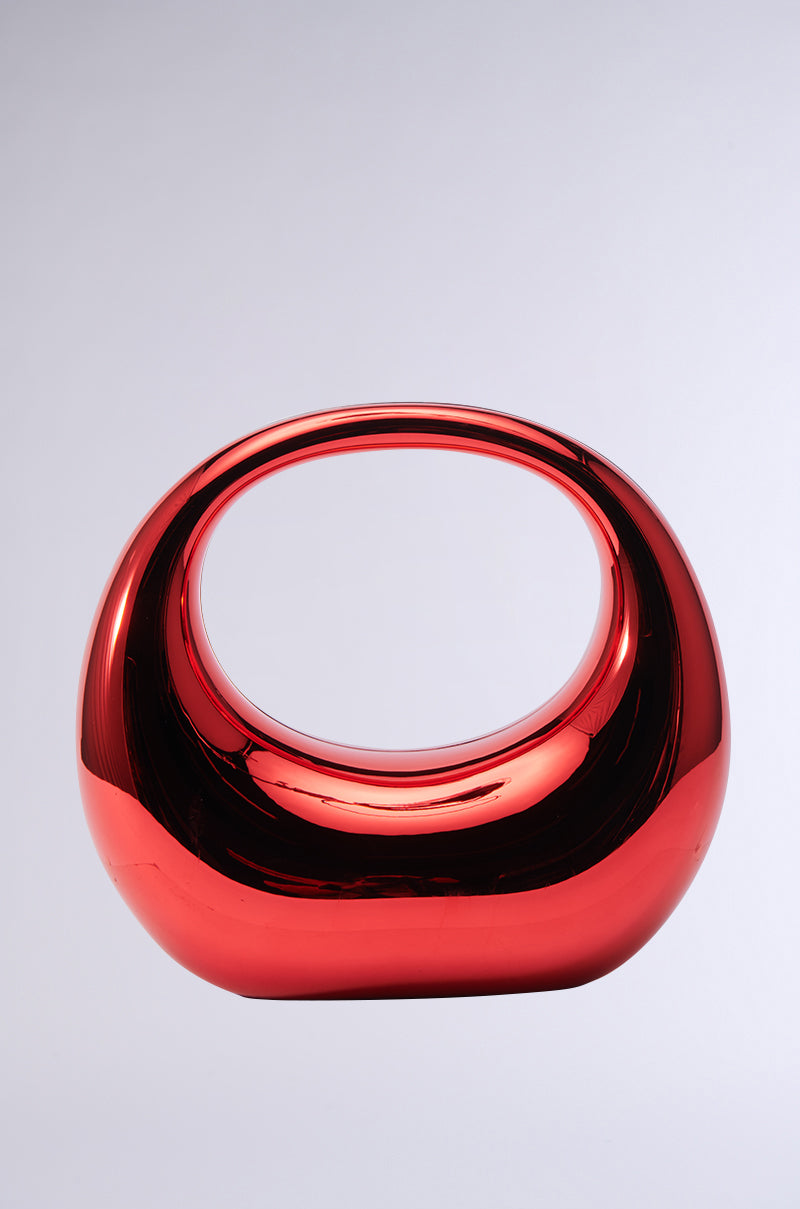Introducing the CHERRY ON TOP CHROME PURSE, a shiny red abstract accessory in the form of a hollow oval with rounded edges, featuring reflective chrome surfaces that stand out against a plain background. 1