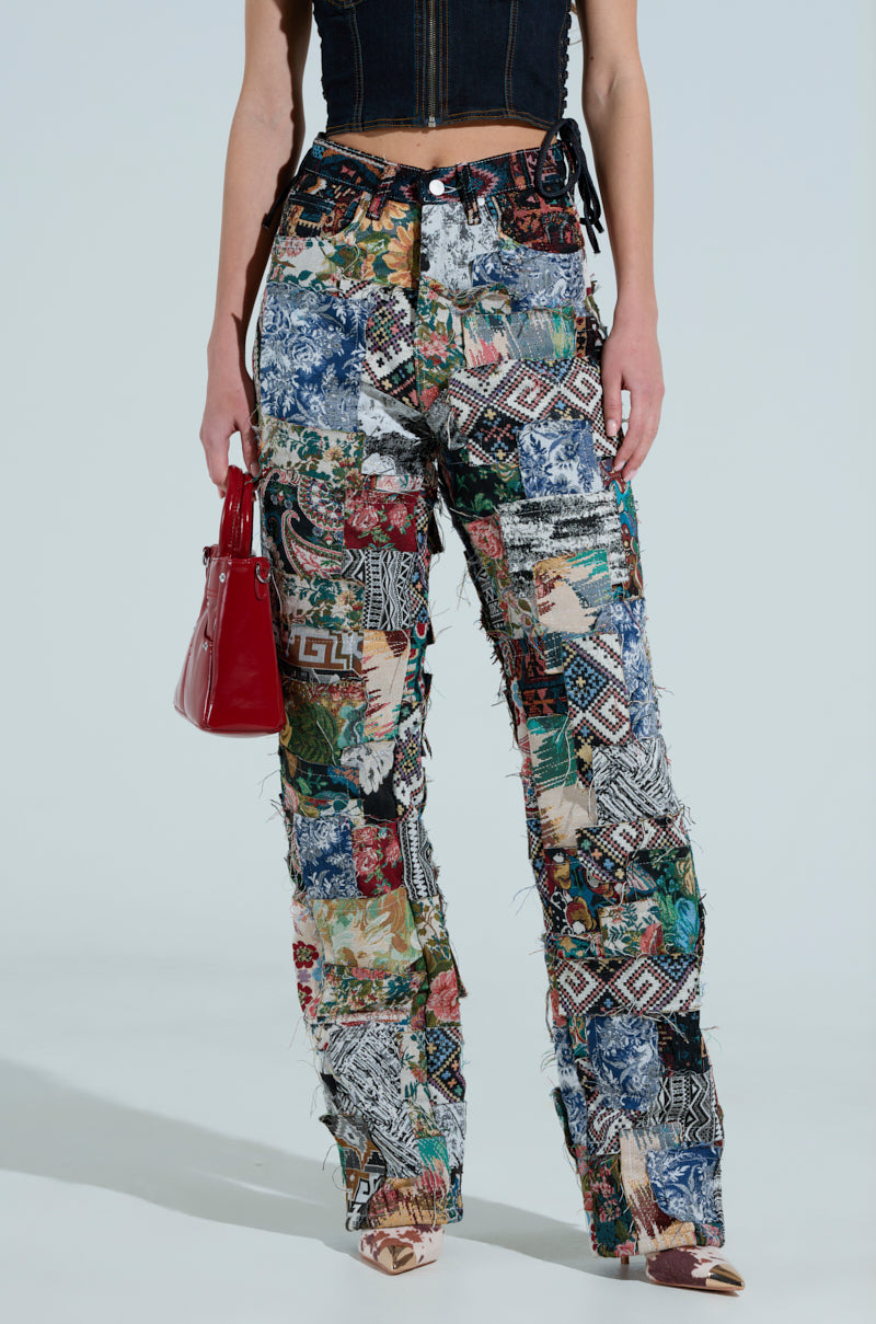 Someone is wearing ODESSA RELAXED FIT PATCHWORK PANTS with a colorful, quilt-like pattern, paired with a red handbag and a dark sleeveless top.