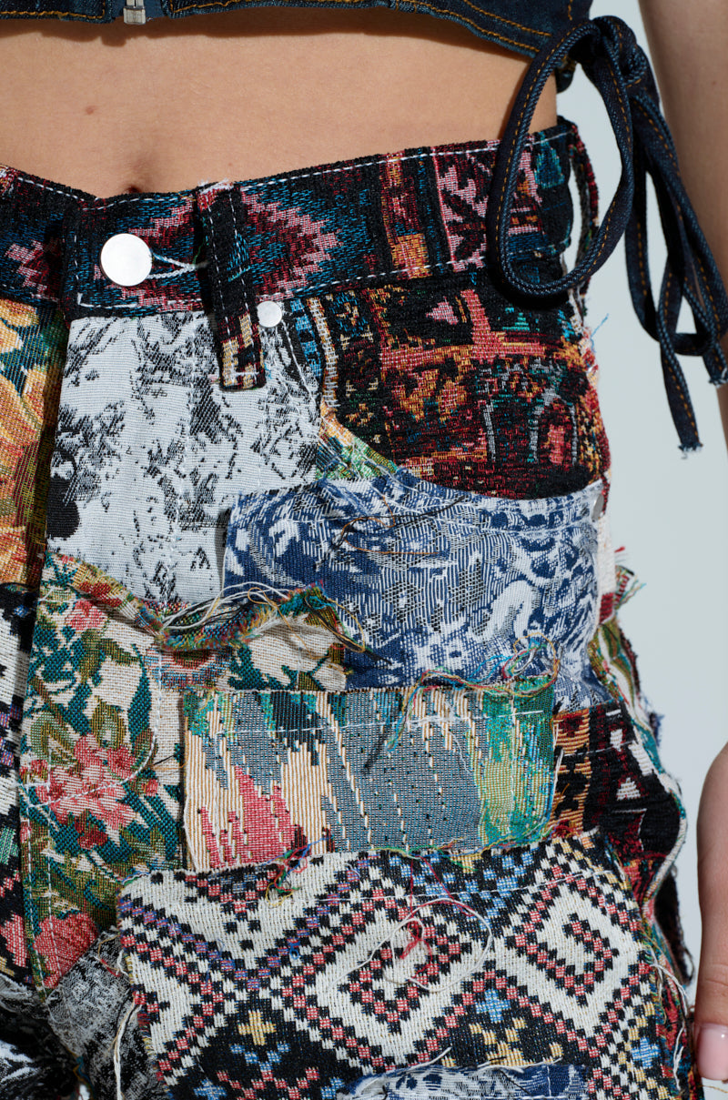 Close-up of the ODESSA RELAXED FIT PATCHWORK PANTS, featuring a patchwork design with colorful floral, geometric, and abstract fabrics. The tapestry-like material is highlighted by a metal button at the top.
