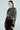Against a plain background, a person with long hair models the DEMI EMBELLISHED MOTO jacket paired with a black lace skirt featuring floral patterns, looking to the side.