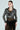 A woman exudes confidence in the DEMI EMBELLISHED MOTO jacket over a black lace dress. She stands against a plain background, her hair slicked back, wearing large hoop earrings with her hands resting by her sides.