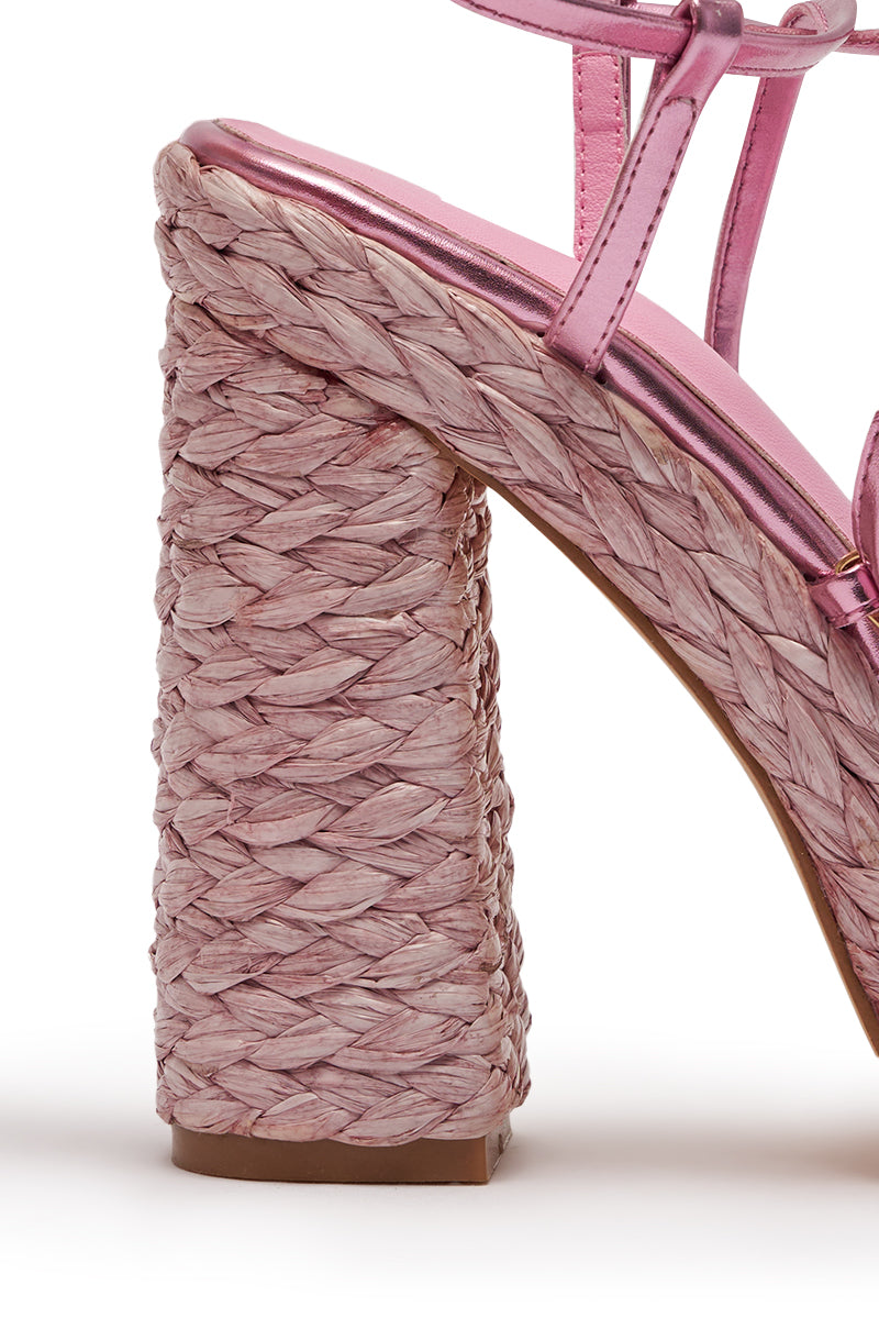 Close-up of the AKIRA GOLD ZAIDEE PINK PLATFORM RAFFIA LACE UP SANDAL featuring pink metallic straps and a thick, woven raffia block heel, angled to display the heel and sole against a white background. 7