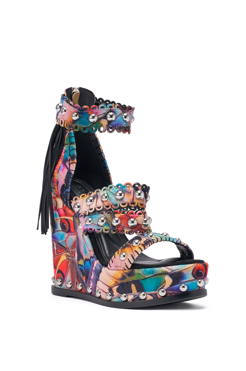 The AKIRA GOLD ZANIA BUTTERFLY MULTI PRINT FRINGE EMBELLISHED WEDGE SANDAL features a colorful suede platform, multicolor print, studded straps, metallic and gemstone details, black fringe at the back, and a bold sky-high wedge heel. 5