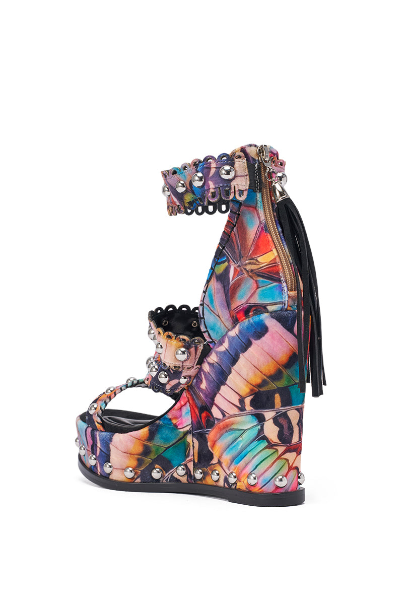 The AKIRA GOLD ZANIA BUTTERFLY MULTI PRINT FRINGE EMBELLISHED WEDGE SANDAL features a colorful butterfly print, ankle strap, beaded and studded details, a black fringe at the heel, and a bold platform wedge for added height. 6