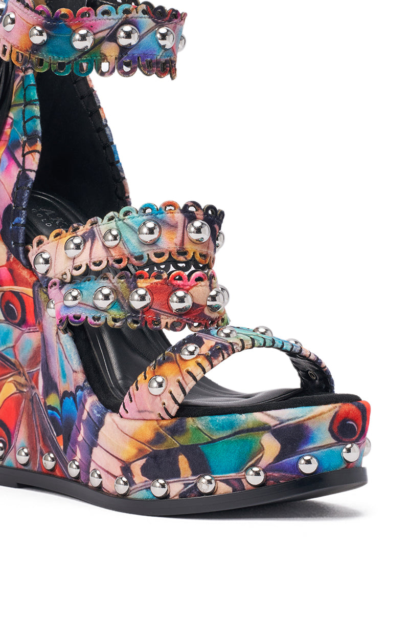 Close-up of the AKIRA GOLD ZANIA BUTTERFLY MULTI PRINT FRINGE EMBELLISHED WEDGE SANDAL, a vibrant suede platform wedge with bold multicolor butterfly designs, multiple straps, fringe details, and shiny silver stud accents. 7