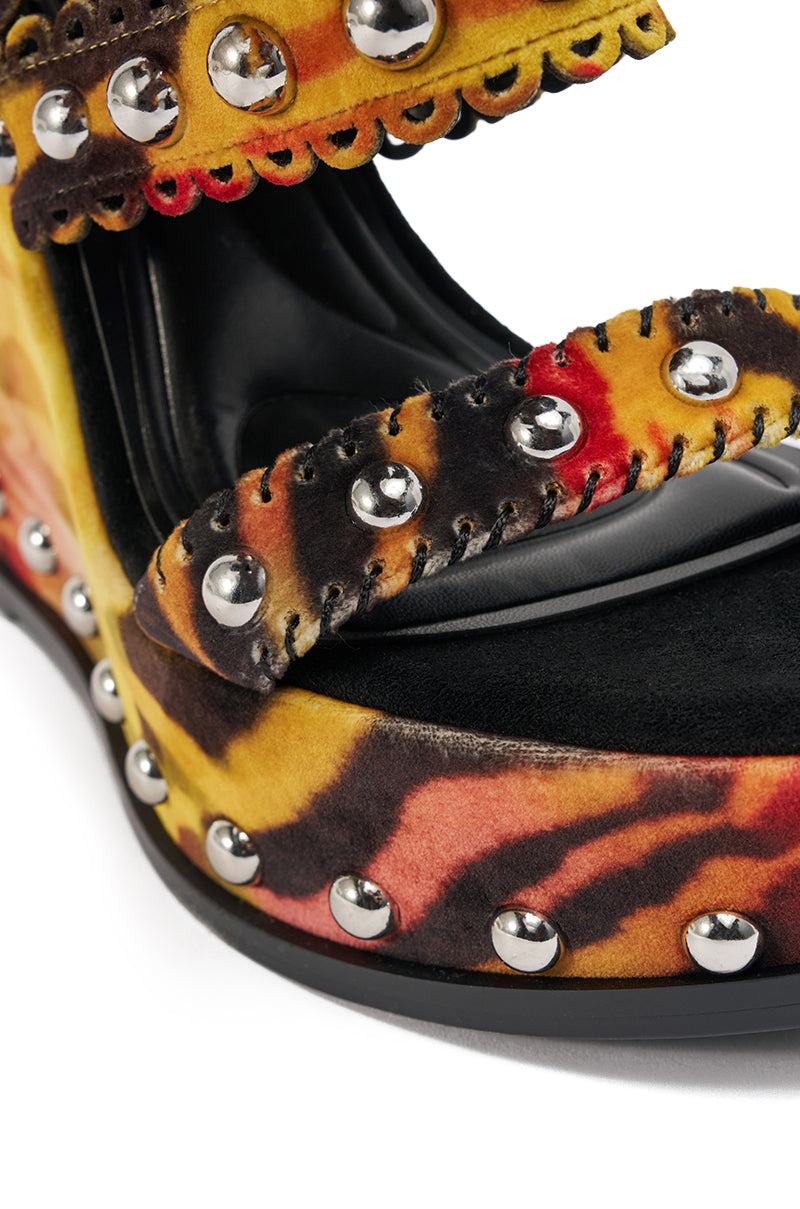 Close-up of the AKIRA GOLD ZANIA TIGER MULTI PRINT FRINGE EMBELLISHED WEDGE SANDAL, featuring vibrant yellow, red, and brown tie-dye fabric, silver studs, and black stitching on thick straps and sole. 7