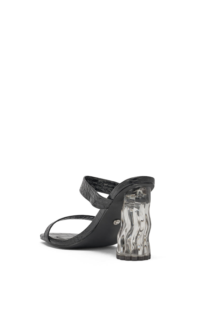 The AKIRA GOLD ZARIA BLACK CLEAR HEEL SLIP ON SANDAL is a black faux leather sandal with two straps and a distinctive wavy clear acrylic chunky heel, shown from the back on a white background. 4