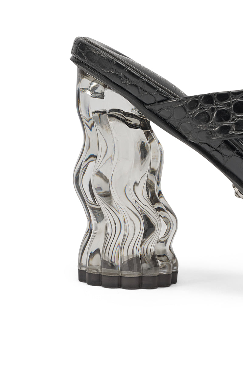 A close-up of the AKIRA GOLD ZARIA BLACK CLEAR HEEL SLIP ON SANDAL shows its black crocodile-embossed faux leather upper and a wavy, transparent chunky heel that gives a striking, luxe look. 5