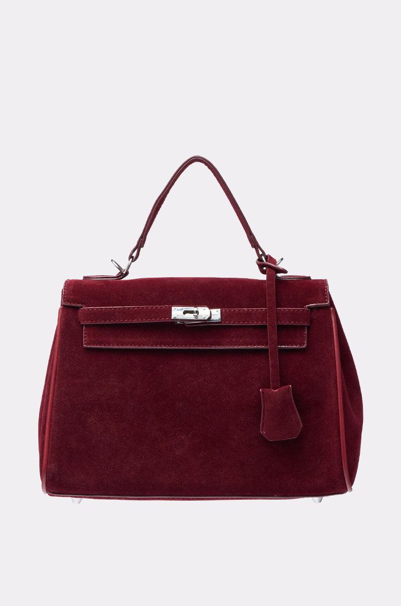 The TAKE ME TO DINNER SUEDE BAG is a burgundy faux suede structured handbag with a top handle, flap closure, silver clasp, and a decorative leather strap, making it a versatile choice for any evening occasion. 0