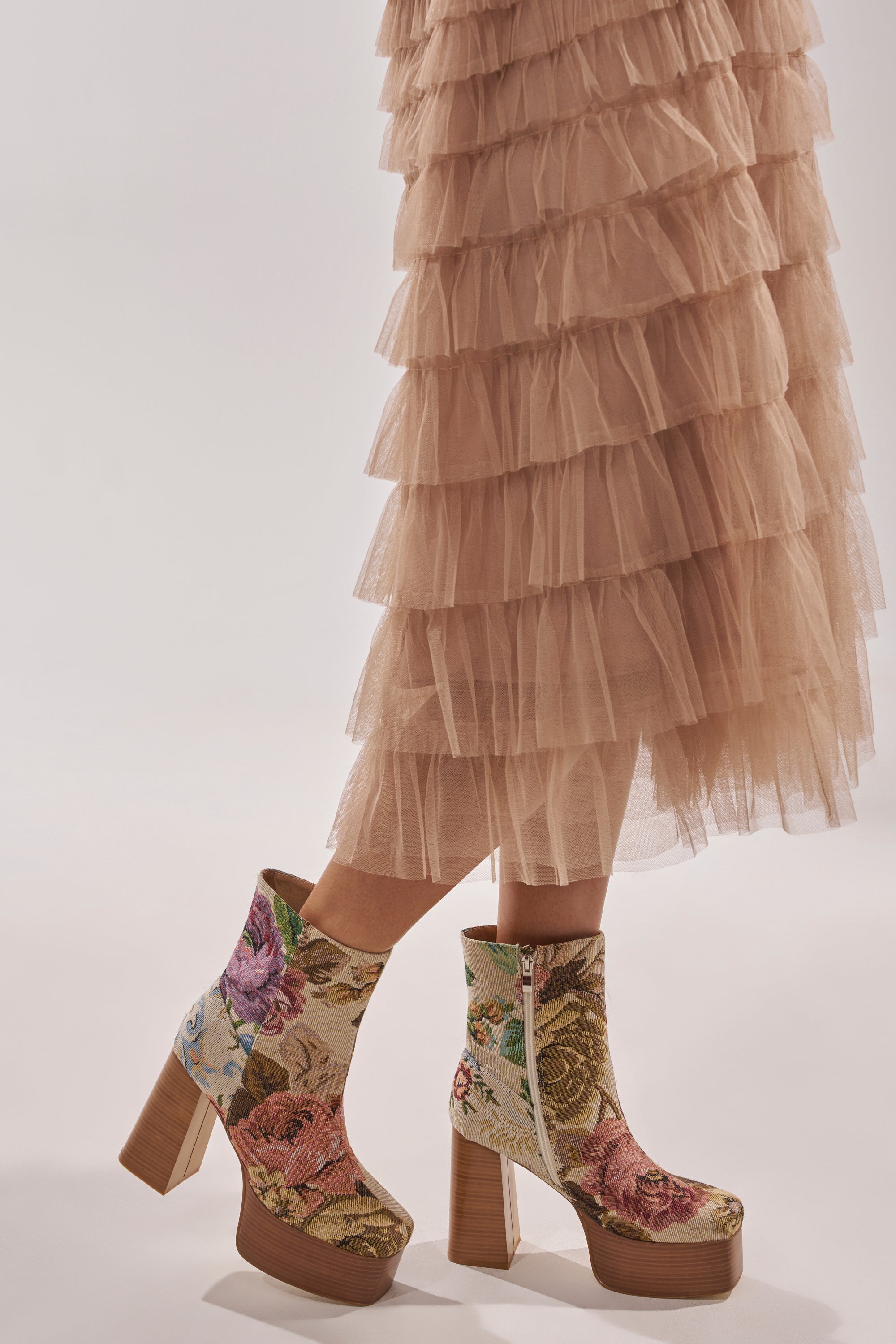 A person wears a tiered blush pink tulle skirt and AZALEA WANG ZILPAH FLORAL BROCADE BOOTIE with chunky block heels, posing against a light background. 1