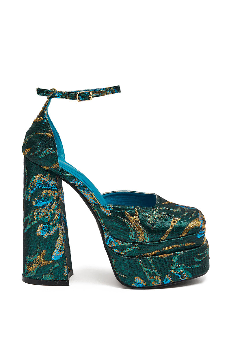 The AZALEA WANG ZIPPHORA BLUE BROCADE CHUNKY PUMP features a blue brocade upper with green fabric, gold and blue floral patterns, an ankle strap, a chunky block heel, and a vibrant blue inner lining.