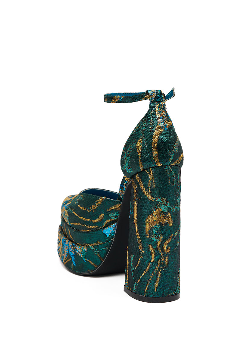 The AZALEA WANG ZIPPHORA BLUE BROCADE CHUNKY PUMP features a high heel, platform sole, ankle strap, and a vibrant green, gold, and blue brocade pattern, shown from the back.