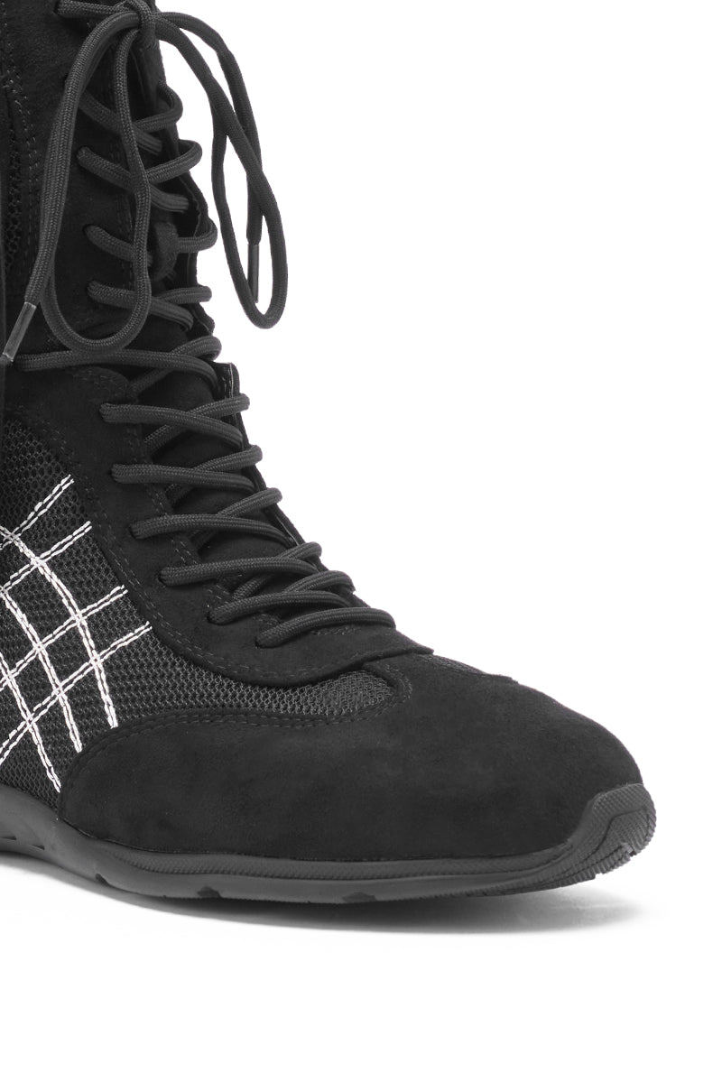 Close-up of the AZALEA WANG ZITHER BLACK FLAT FRINGE BOOTIE, a black lace-up ankle boot with white stitched side patterns, a textured rubber sole, and a stylish mix of suede and mesh materials.