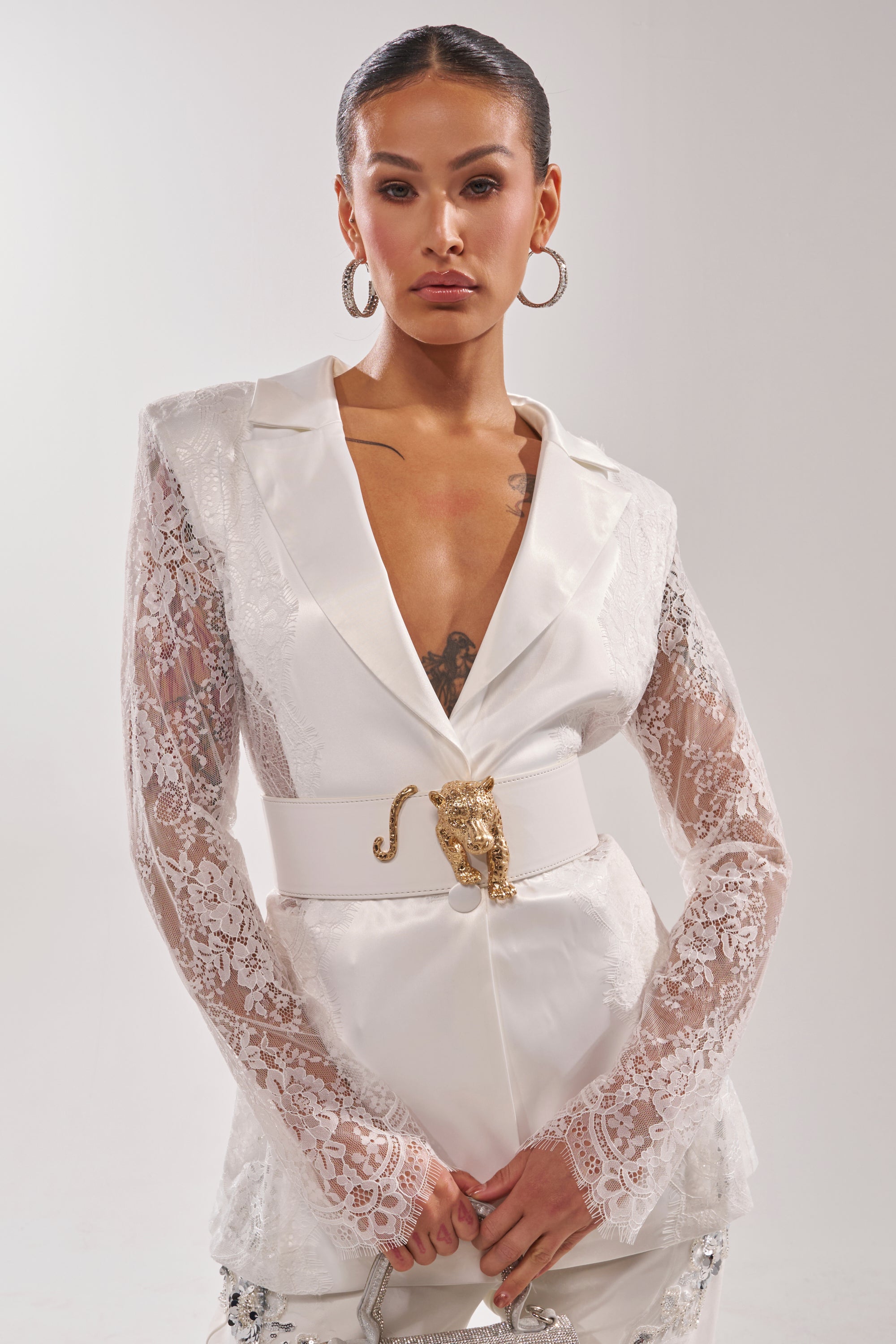 A woman in a white dress elevates her style with the NO BOUNDARIES PU STRETCH BELT IN WHITE, adding a touch of modern flair to her elegant outfit. 1