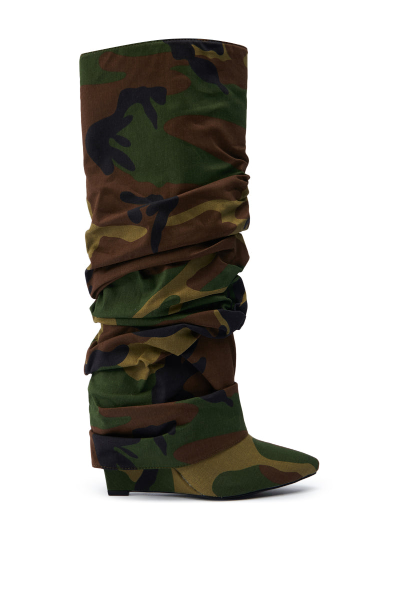 The AZALEA WANG ZUMMA CAMO WEDGE BOOT is a chic knee-high with a scrunched camo pattern in green, brown, and black. It boasts a pointed toe and low wedge heel on a clean white backdrop.