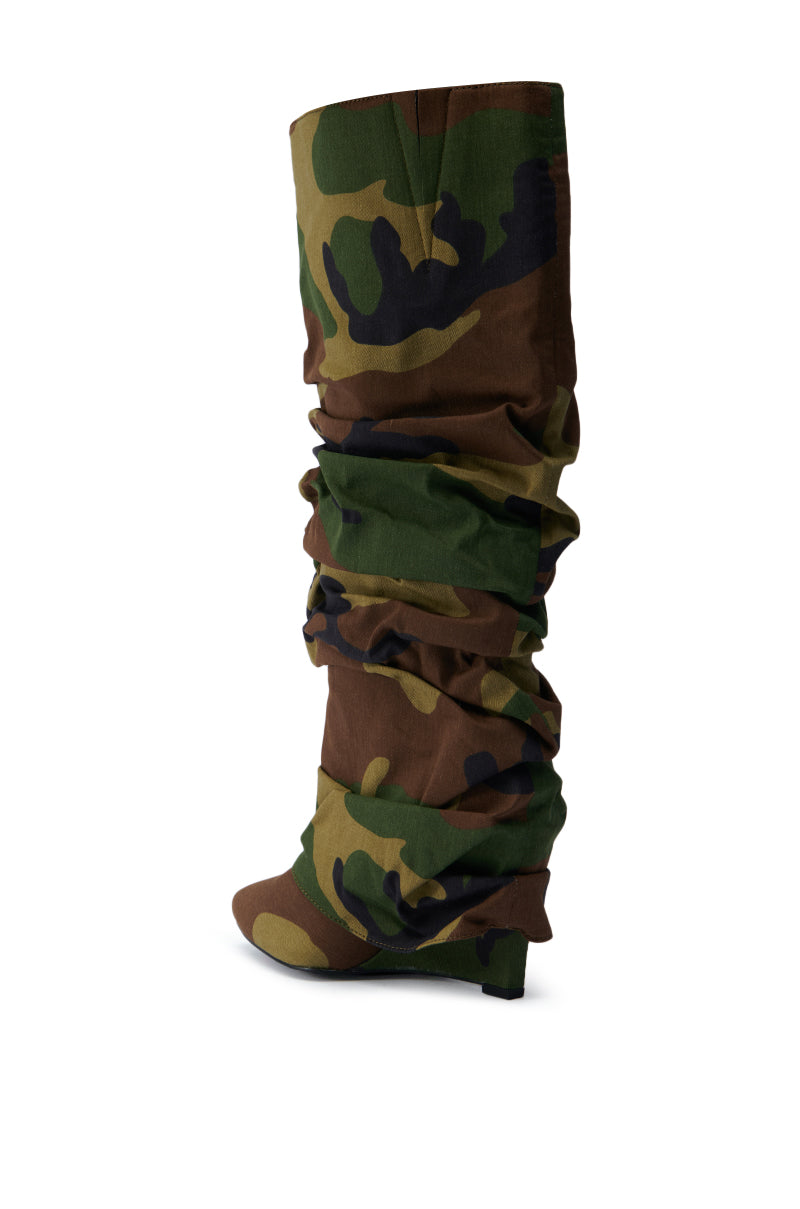The AZALEA WANG ZUMMA CAMO WEDGE BOOT, featuring a slouchy and wrinkled design in green, brown, and black camouflage with a pointed toe and small heel, is showcased against a plain white background.