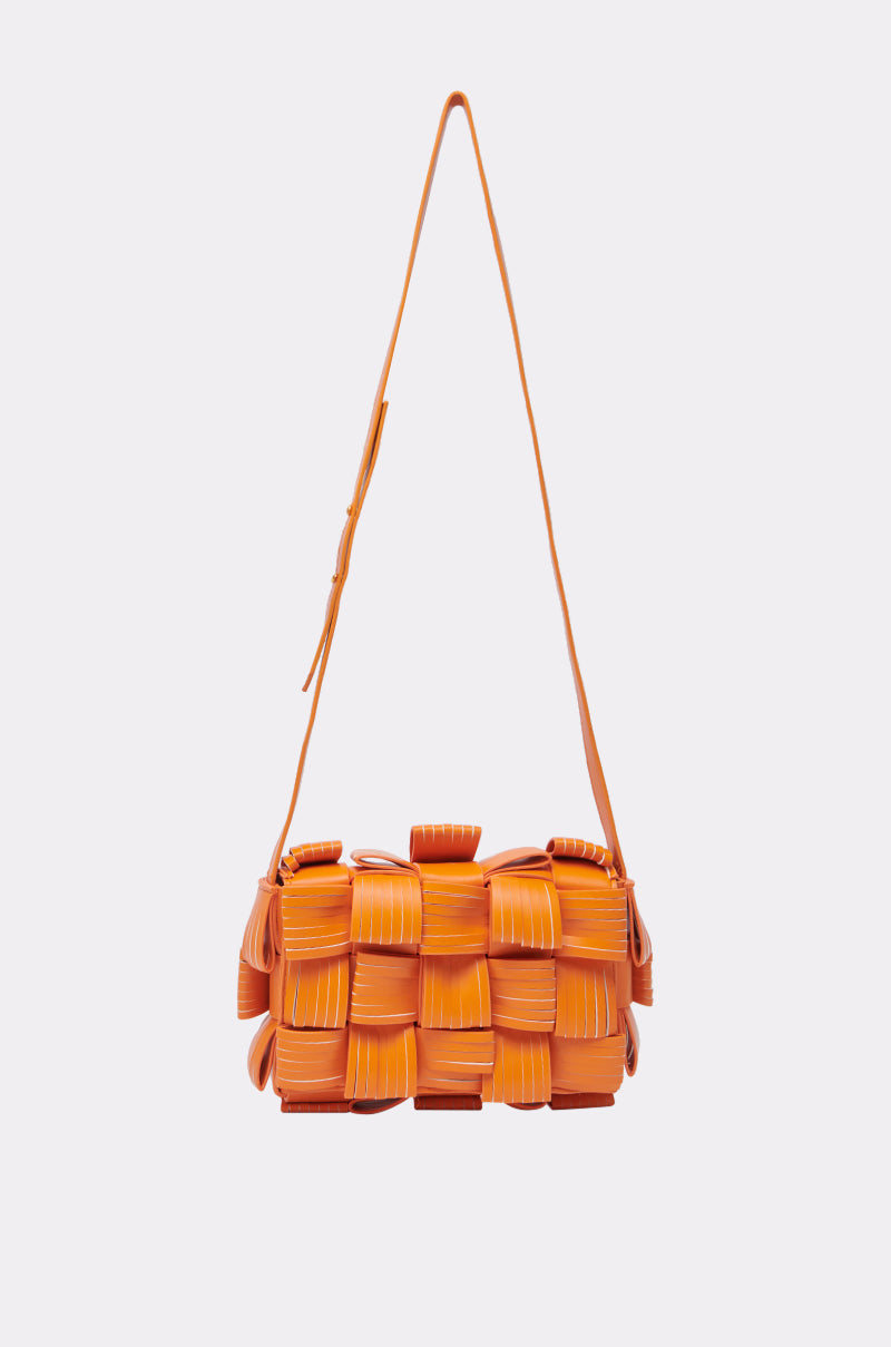 The ORANGE YOU GLAD? PURSE is a bright orange rectangular faux leather crossbody bag featuring a unique woven pattern and a matching adjustable shoulder strap, shown on a plain light gray background.