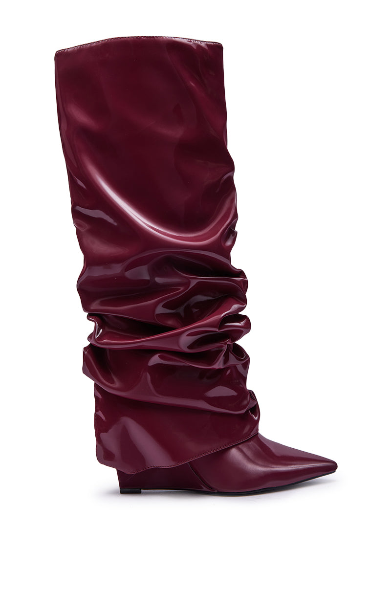 The AZALEA WANG ZYLLA Burgundy Patent Wedge Ruched Boot is shown side view, knee-high with a shiny finish, pointed toe, low wedge heel, and ruched fold-over design against a white background.