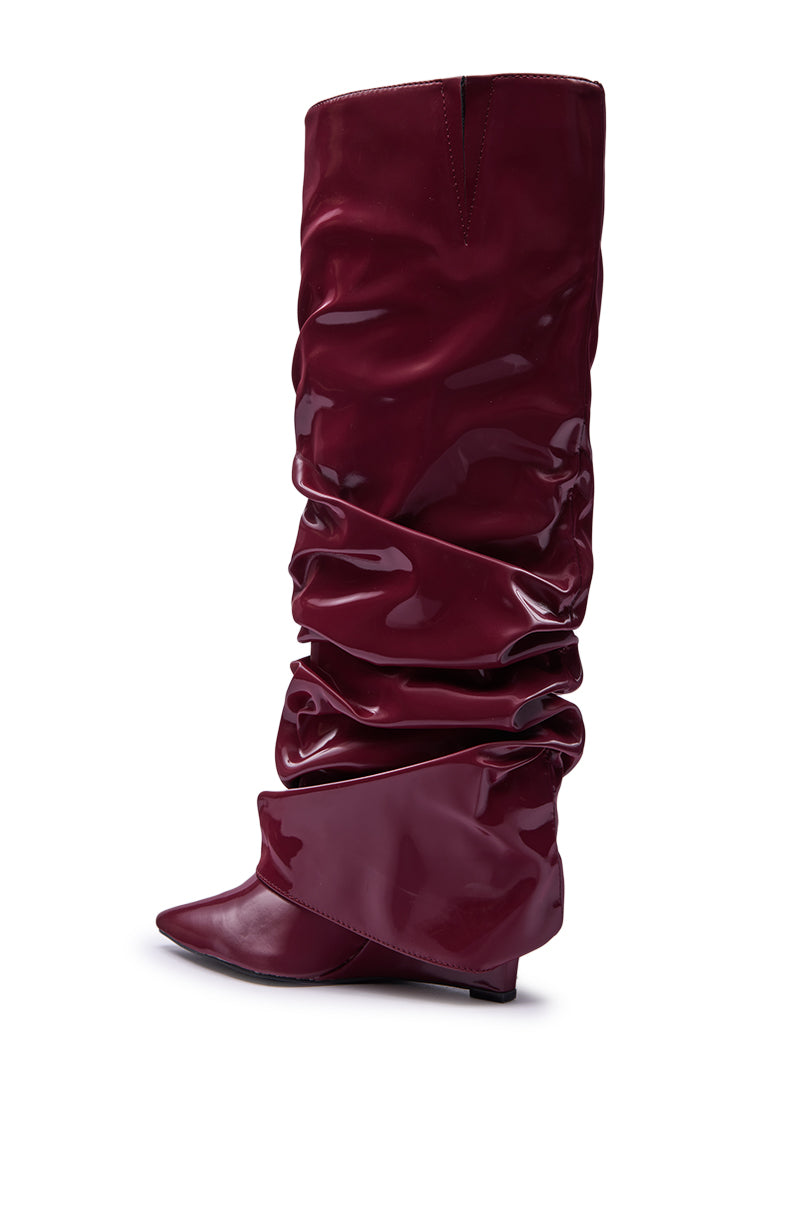 The AZALEA WANG ZYLLA BURGUNDY PATENT WEDGE RUCHED BOOT is a tall, knee-high, slouchy boot in glossy faux patent leather with a pointed toe, low wedge heel, and ruched detailing, shown against a white background.